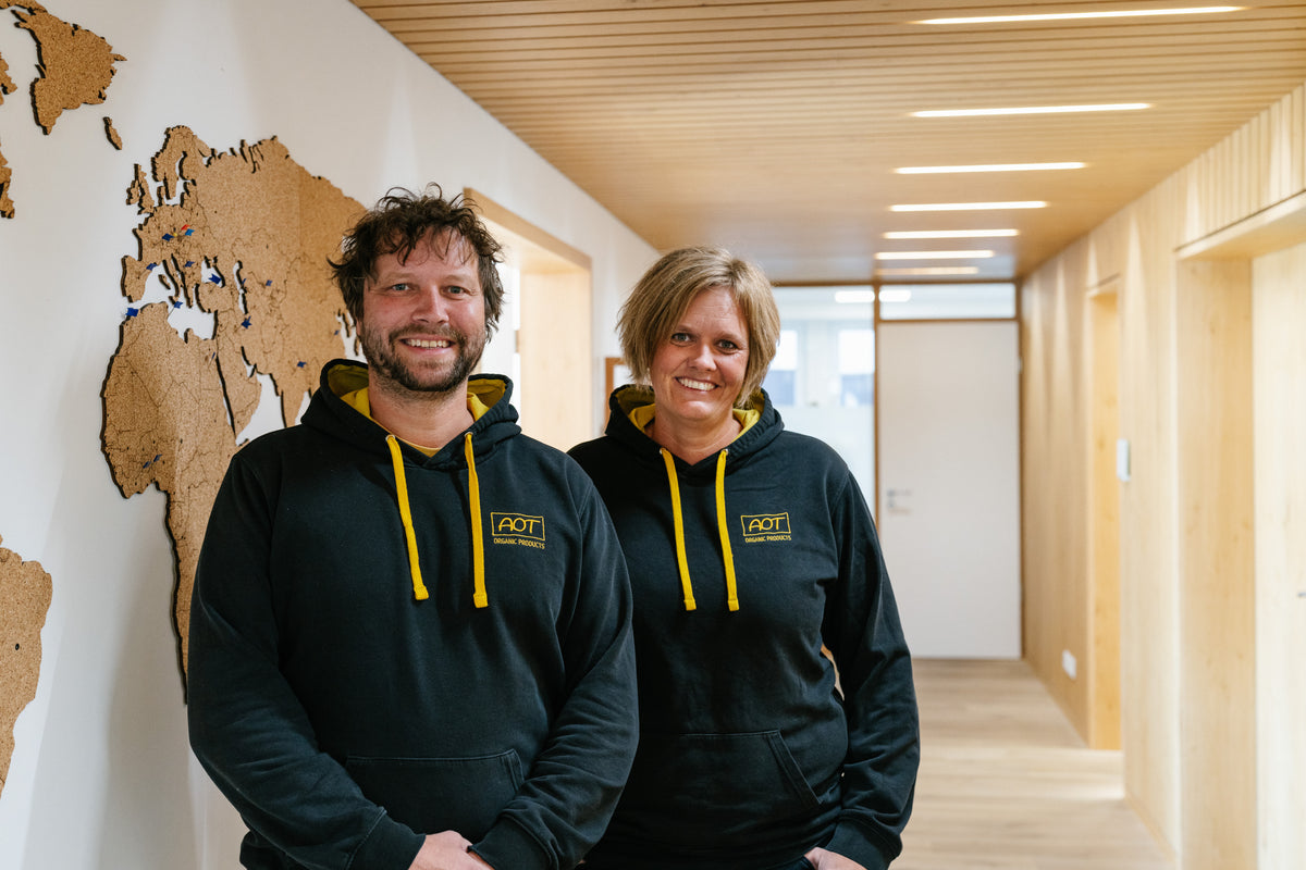 Dos empleados de AOT con sudaderas de la empresa en el pasillo delante de un mapamundi